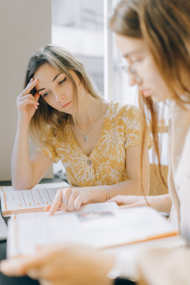 Two women collaborating on study materials in a bright library setting.